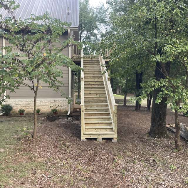 Wide pressure-treated deck stairway with railing leading to a second-story deck