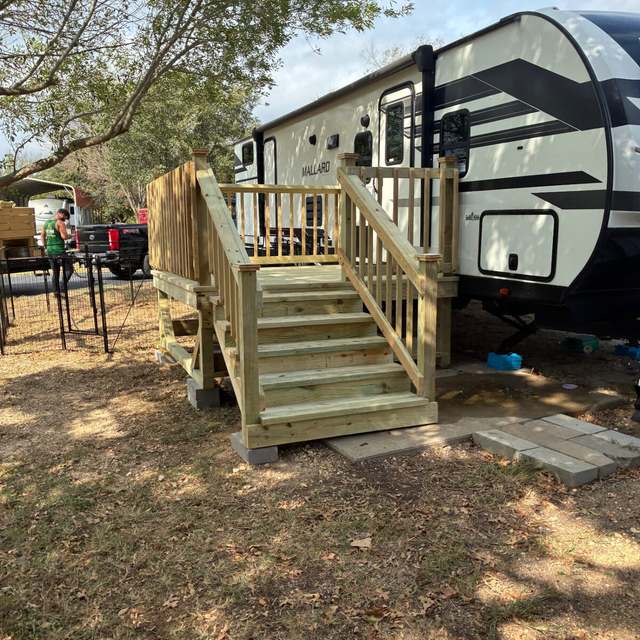 Pressure treated RV entry deck with steps, handrails and spindle railing on blocks beside a travel trailer